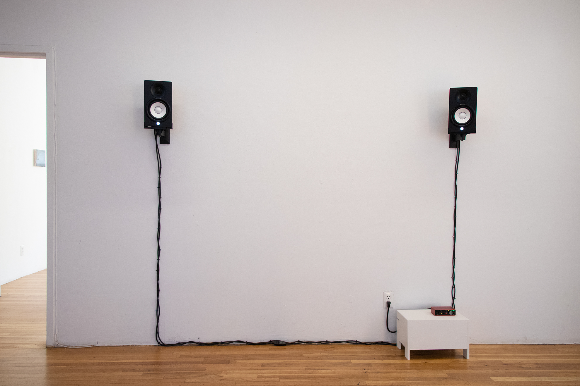 [Two wall-mounted speakers connected to a red mini-amp sitting on a small white stand.]