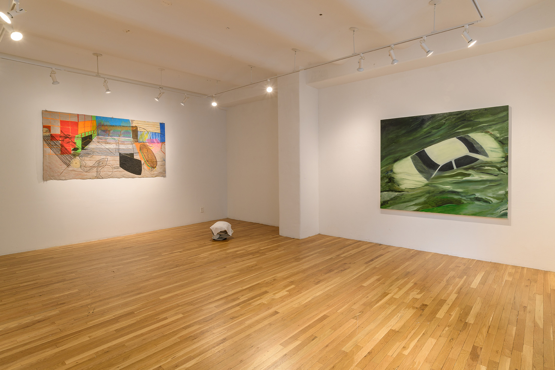 [Two large paintings of cars are hung on adjacent walls. In the corner between them is a white stack of dishes with a cloth draped over them.]