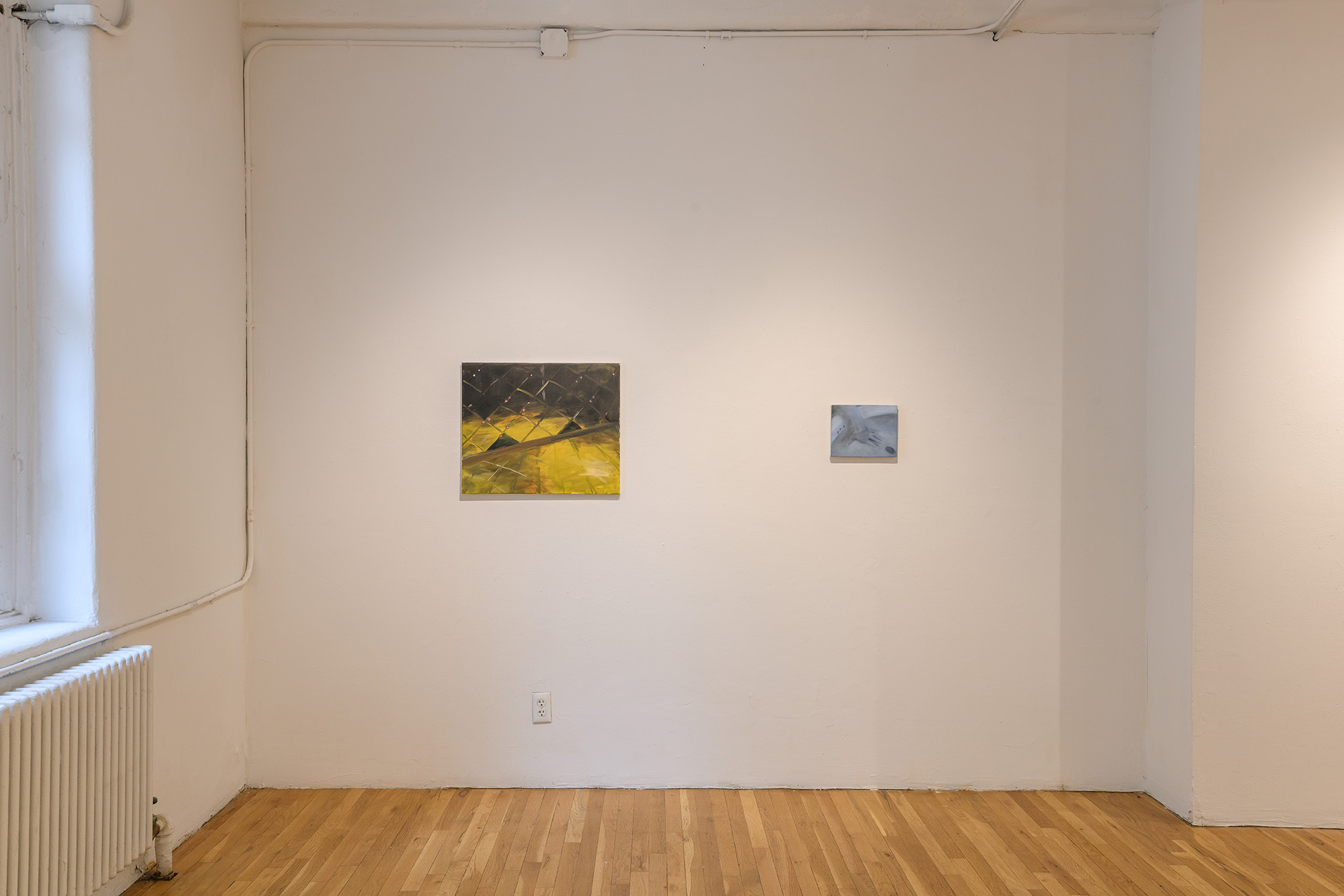[Two paintings hanging on a white wall hear a window. The painting on the left, rendered in yellows, acid greens, and blacks, is slightly larger than the painting on the right, which is rendered in blues and grays.]