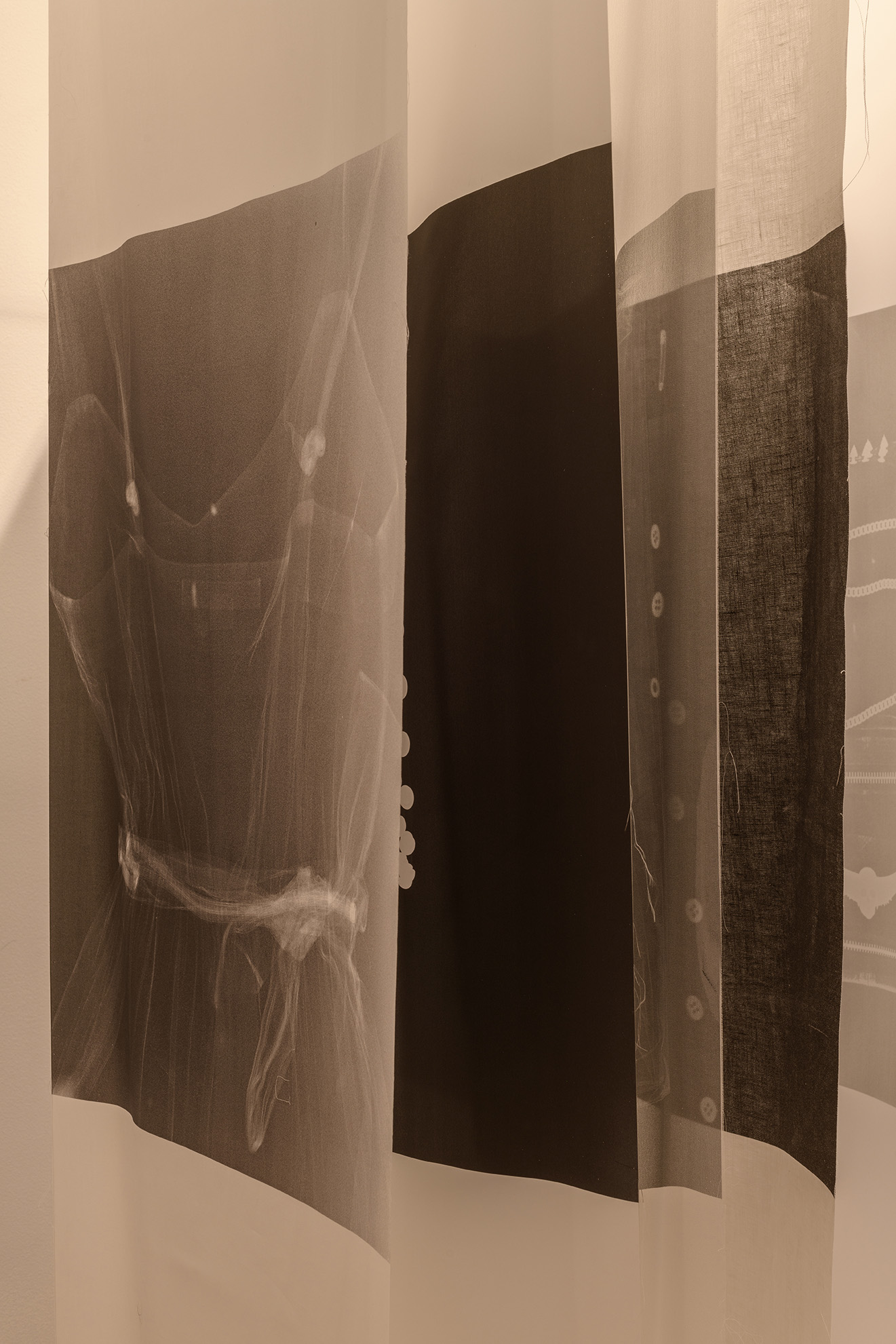 [The x-ray prints are visible through the silk backing material, and it is apparent that the stack is arranged face-to-face, back-to-back. The faint outline of a dress with a ribbon faces a collection of stark white dots belonging to a garment it is difficult to identify by x-ray alone.]